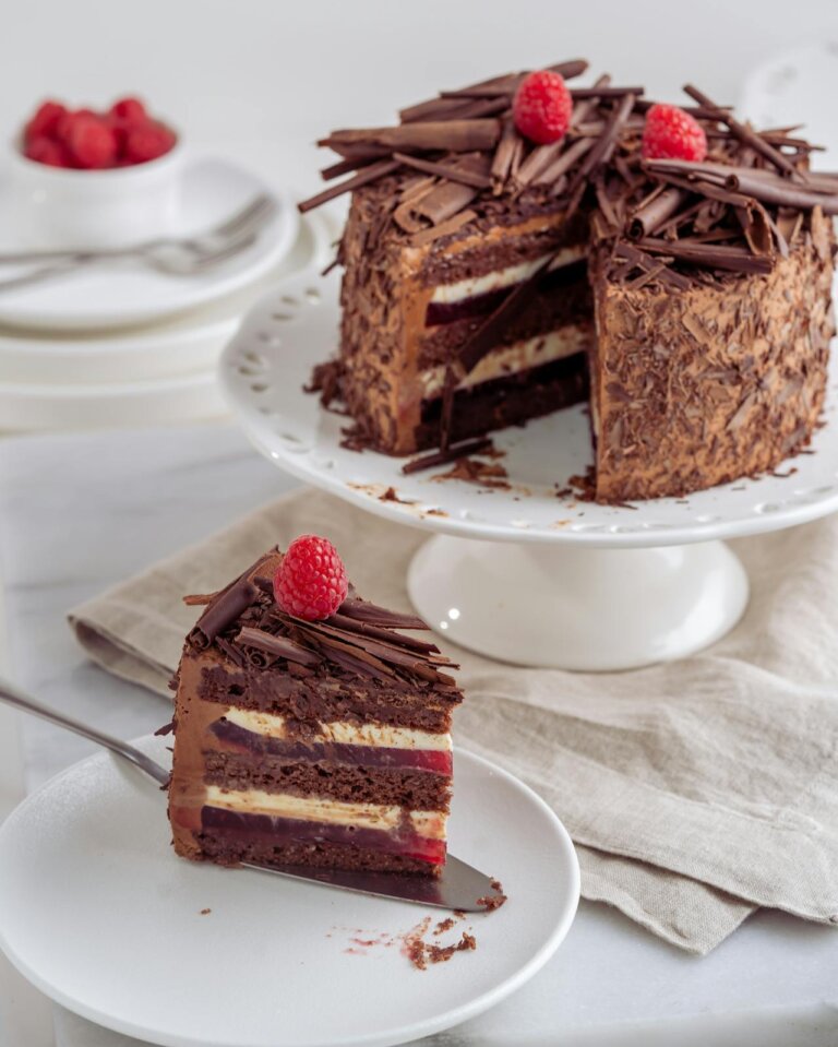 three layered blackforest cake topped with chocolate shavings and raspberries, a sclice kept on a plate aside.