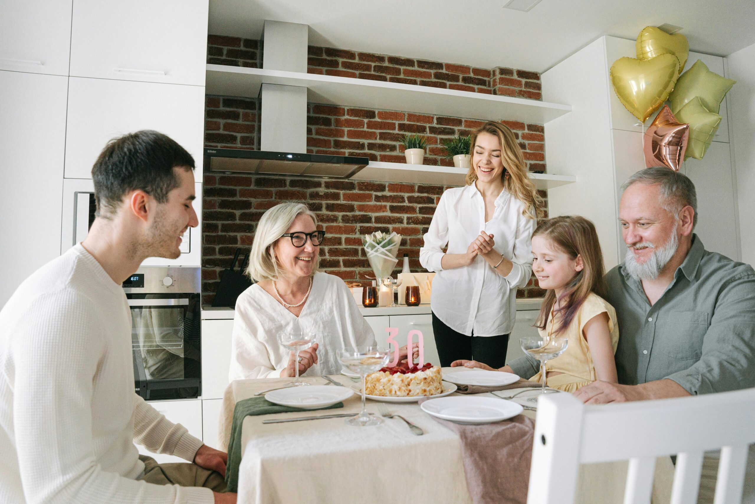 Family celebrating with a Mother's Day cake at home, gathered around the dining table with balloons, smiles, and a joyful atmosphere.