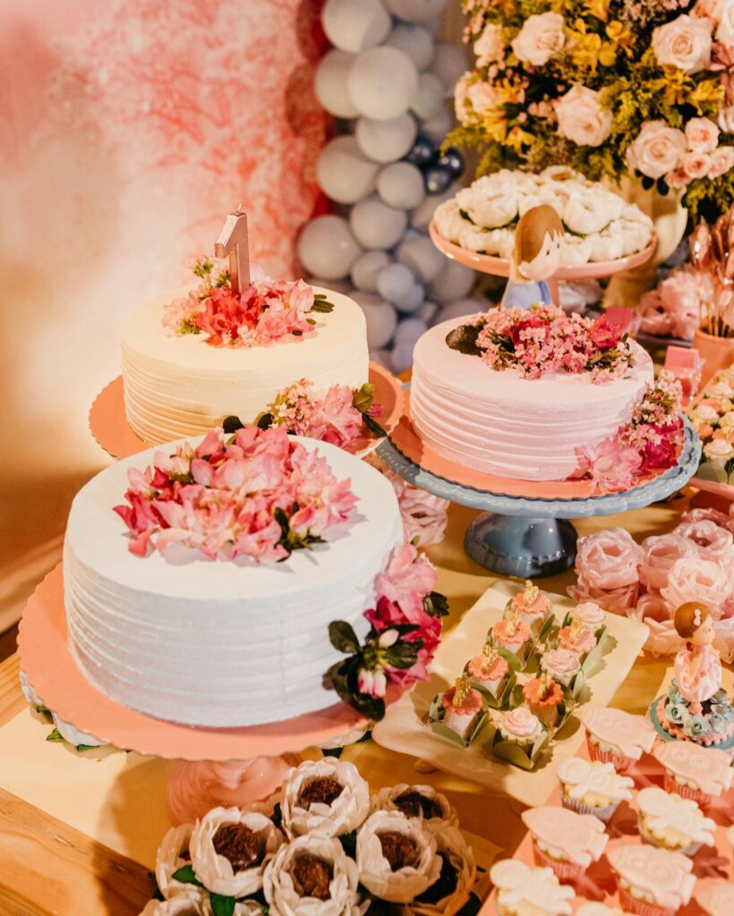 floral themed birthday cakes for a one year old's birthday celebration. there are three white frosting cakes decorated with flowers to match the floral theme.