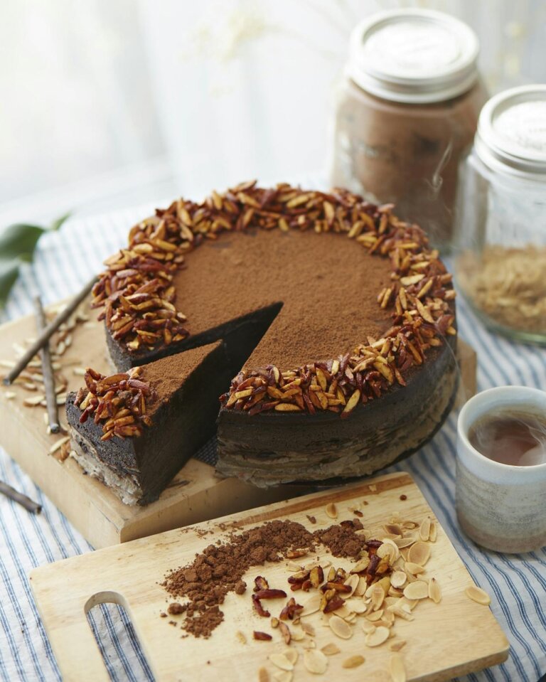 rich chocolate fudge cake placed on a cutting board, topped with some chopped nuts