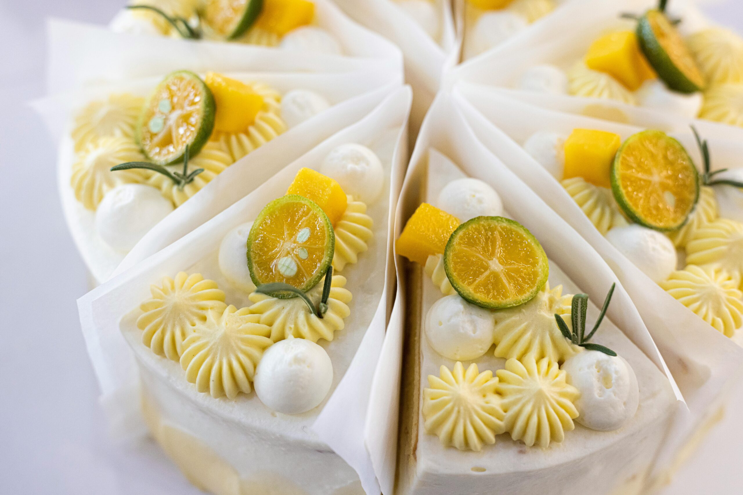 Bakery - slices of lemon cake placed together like a whole cake. each piece has got white and yellow decorations made with whipped cream along with a slice of fresh lime and a herb.