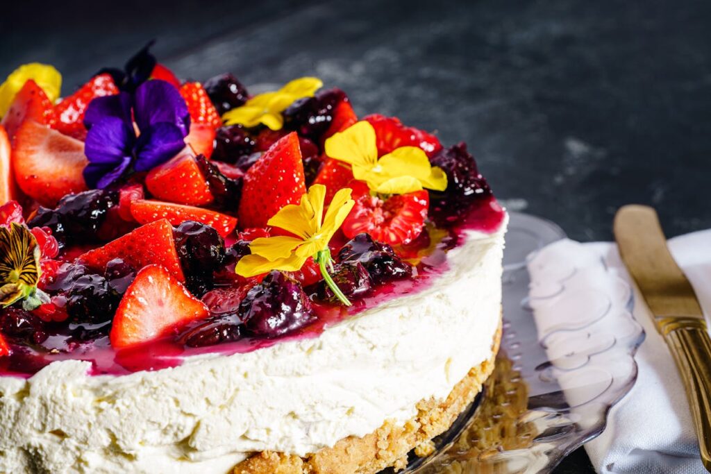 This image shows a freshly baked cake with strawberry, blueberry on top with flowers as decoration perfect for Summer cakes collection.