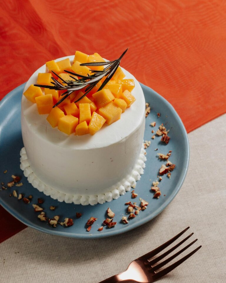 mango cake in a plate topped with fresh mango pieces and a till.